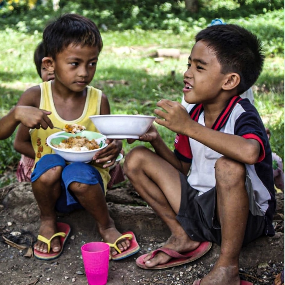 Two young children sharing a meal outdoors in Manila, Philippines